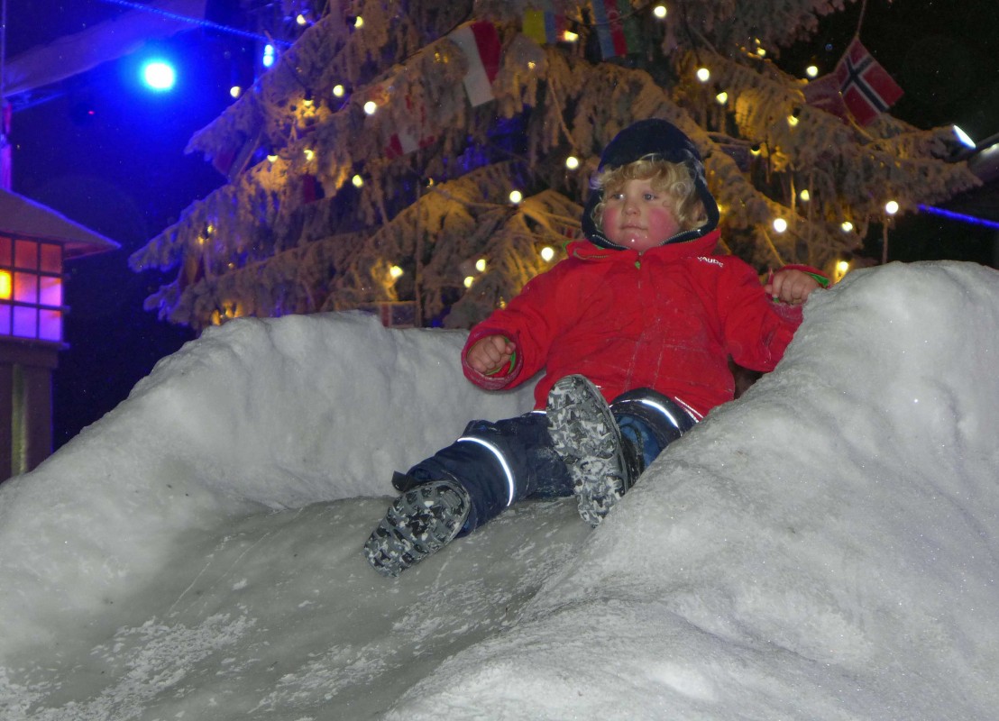 Kind rutscht auf einem Schneeberg hinunter